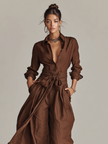 Full-body view of FJØRNA cotton-linen women’s jumpsuit with shirt collar, long sleeves, wide-leg pants, and belt in brown.