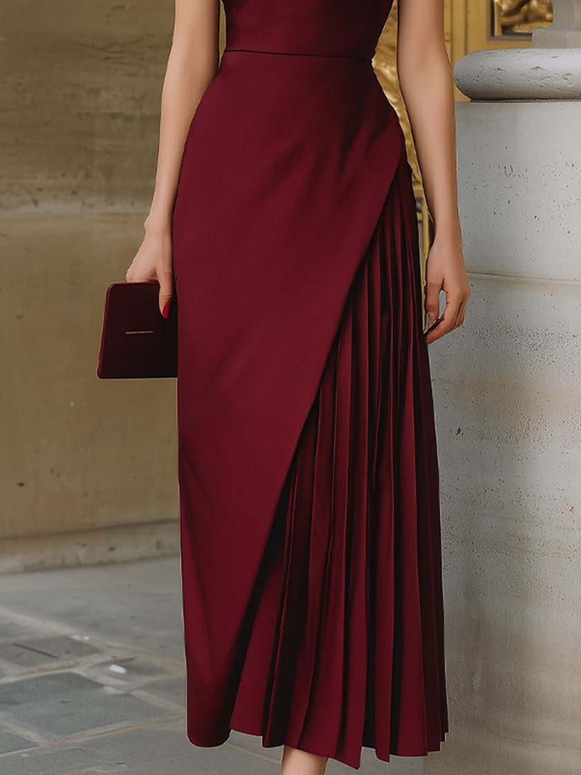 FJØRNA burgundy halter-neck asymmetric pleated midi dress displayed on a model, showcasing its elegant design and flowy fabric.