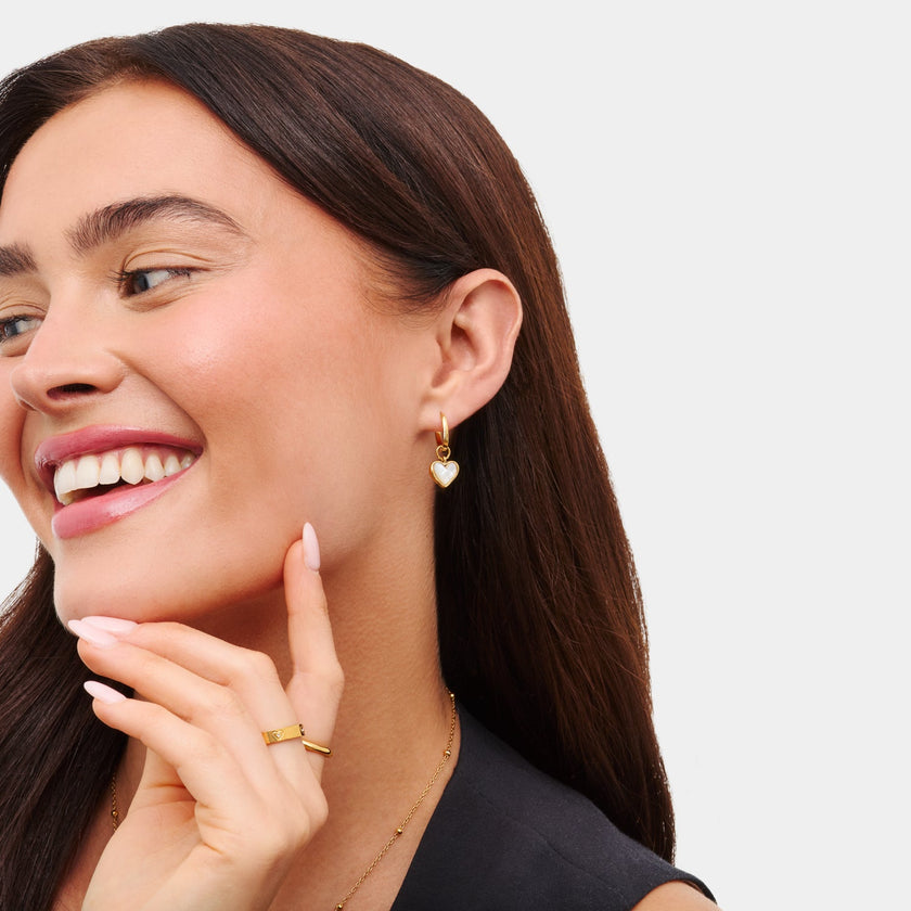 White quartz heart huggie earrings by FJØRNA, gold-tone jewelry for women, featuring sleek hoop design with heart-shaped quartz accents.