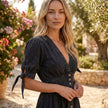 FJØRNA button front midi dress with V-neck and waist tie, shown on a model, featuring a flowing fabric and elegant design.