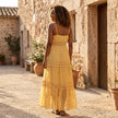 FJØRNA tiered lace maxi dress with V-neck and flowing skirt, shown on a model in a stylish outdoor setting.