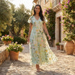FJØRNA floral chiffon maxi dress with short sleeves and V-neck, featuring a colorful floral pattern and flowing fabric.