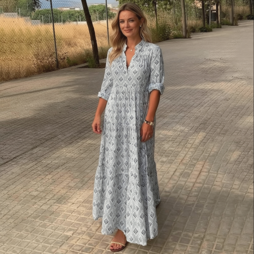 FJØRNA printed long sleeve maxi dress with V-neck, relaxed fit, and flowing fabric, shown hanging on a clothing rack.