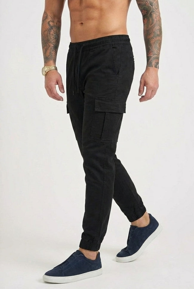 Men's black cargo jogger trousers by FJØRNA with multiple pockets and tapered fit, shown on a model.