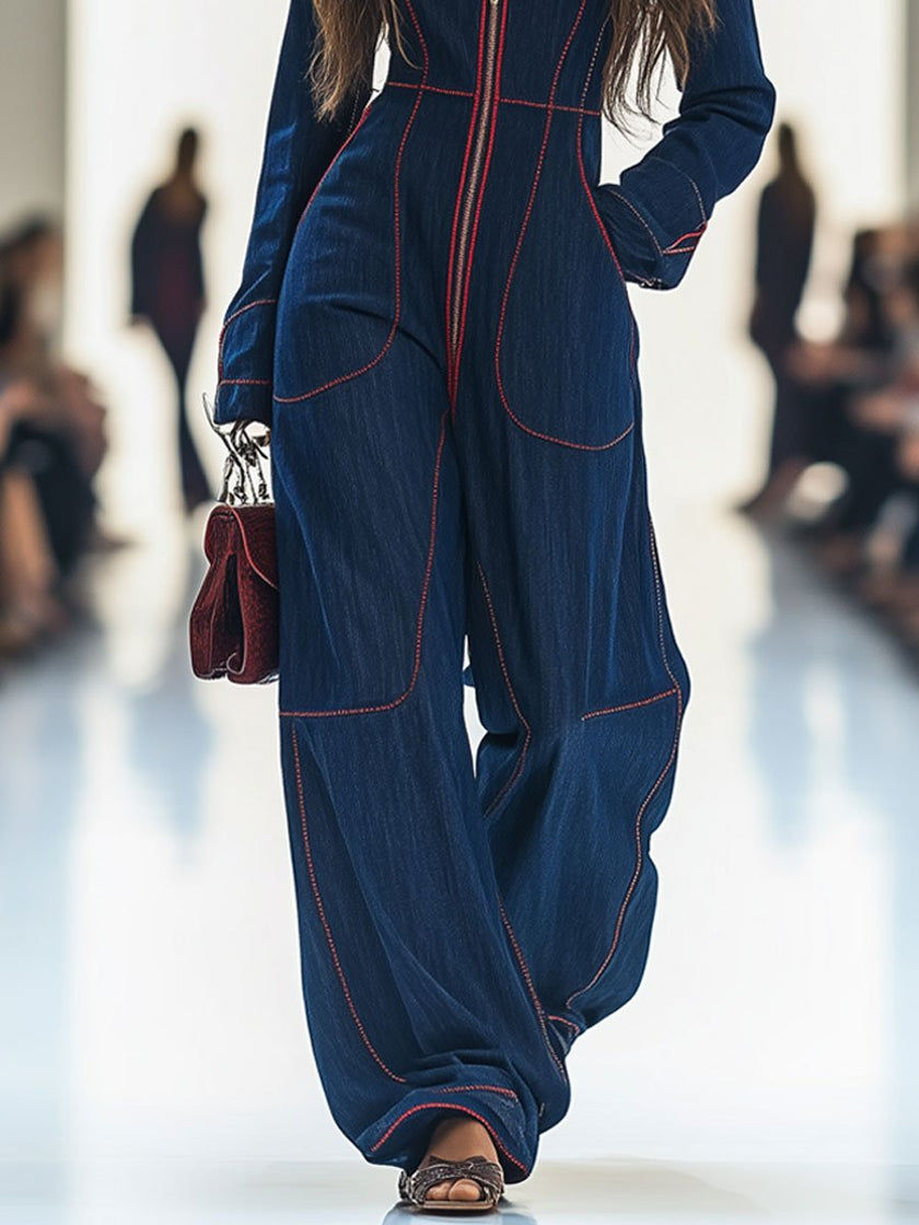 Dark blue FJØRNA denim jumpsuit with topstitching, wide-leg design, long sleeves, and a fitted waist on a model.