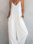 Full-body image of a woman wearing FJØRNA cotton-linen sleeveless jumpsuit with loose fit, square neckline, and wide-leg pants.