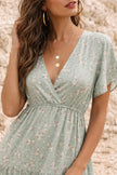 Sage green floral print FJØRNA dress with a flowing silhouette, featuring vibrant flower patterns and lightweight fabric.