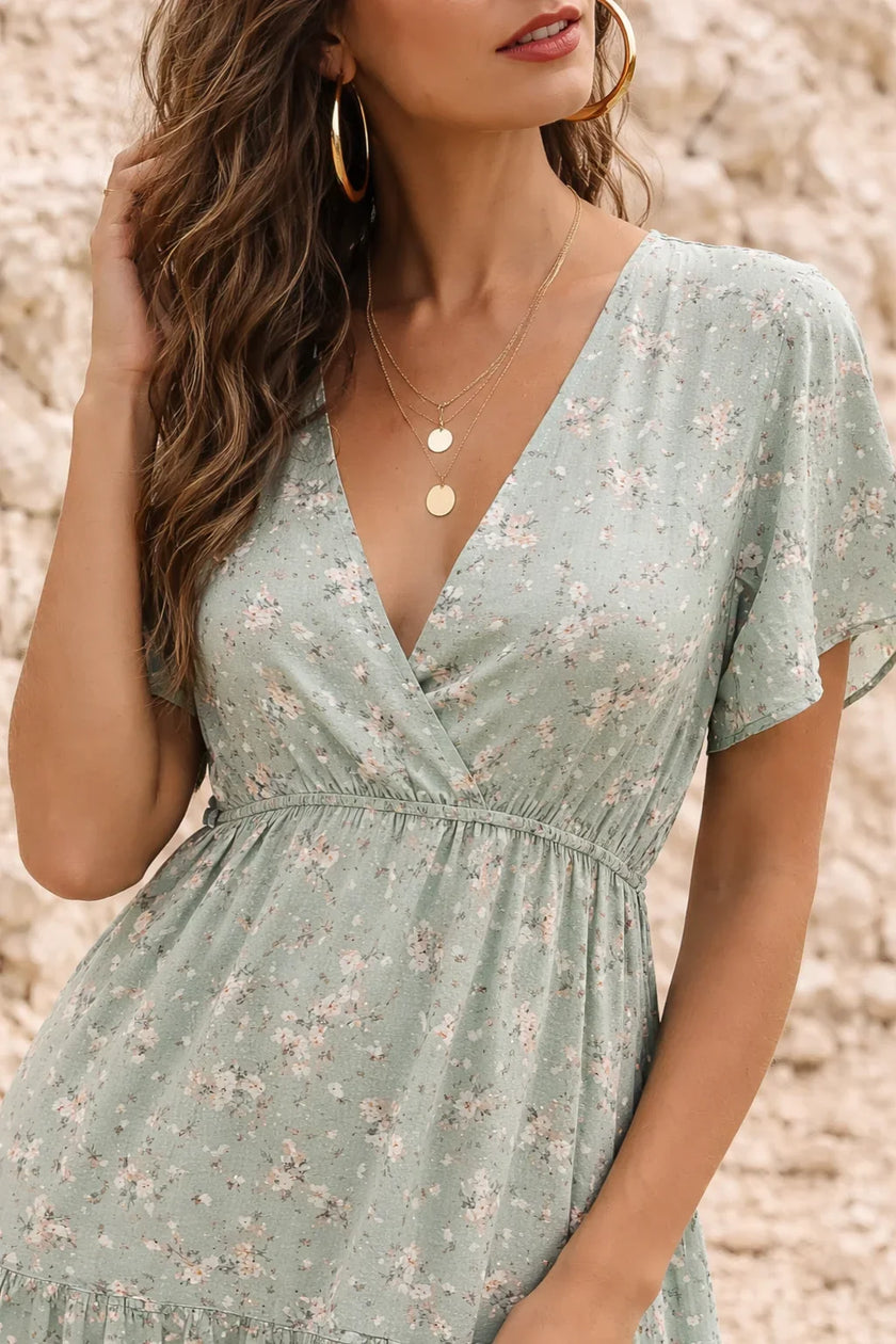 Sage green floral print FJØRNA dress with a flowing silhouette, featuring vibrant flower patterns and lightweight fabric.