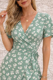 Sage green FJØRNA wrap dress with a front slit, flowing fabric, and elegant silhouette, perfect for stylish occasions.