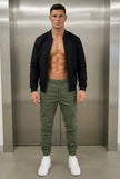FJØRNA cargo jogger trousers in army green, featuring multiple pockets and a relaxed fit, displayed on a model.