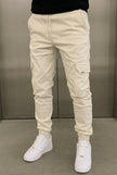 Cream cargo jogger trousers by FJØRNA displayed on a model, featuring relaxed fit, multiple pockets, and casual streetwear style.