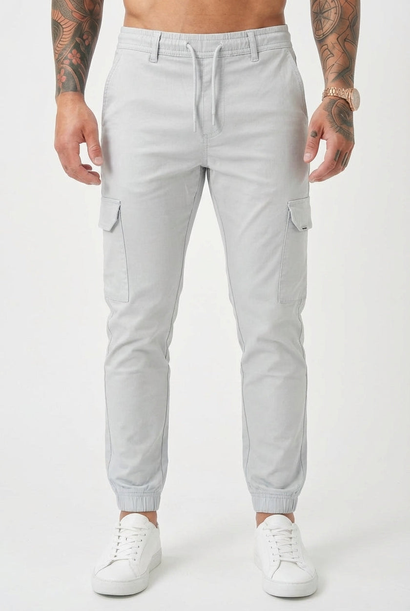 FJØRNA Cargo Jogger Trousers in stone color, featuring relaxed fit and multiple pockets, displayed on a model.