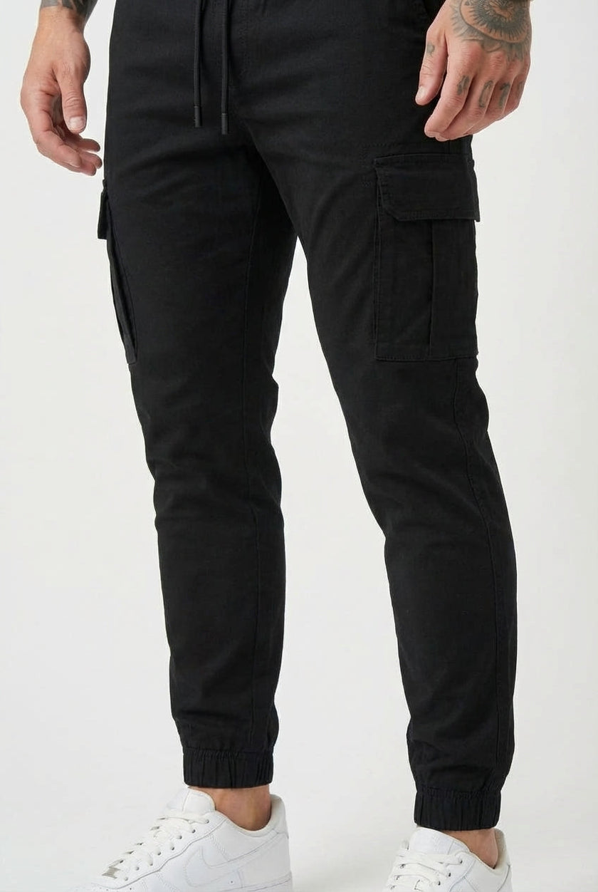 Black FJØRNA cargo jogger trousers displayed on a model, showcasing the relaxed fit and functional pockets.