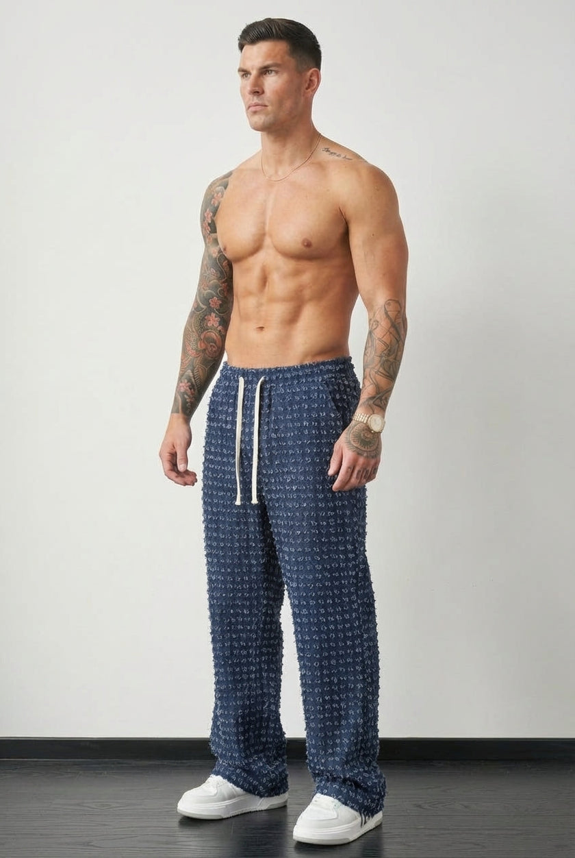 Black distressed trousers by FJØRNA with ripped details and a relaxed fit, shown on a model standing against a neutral background.