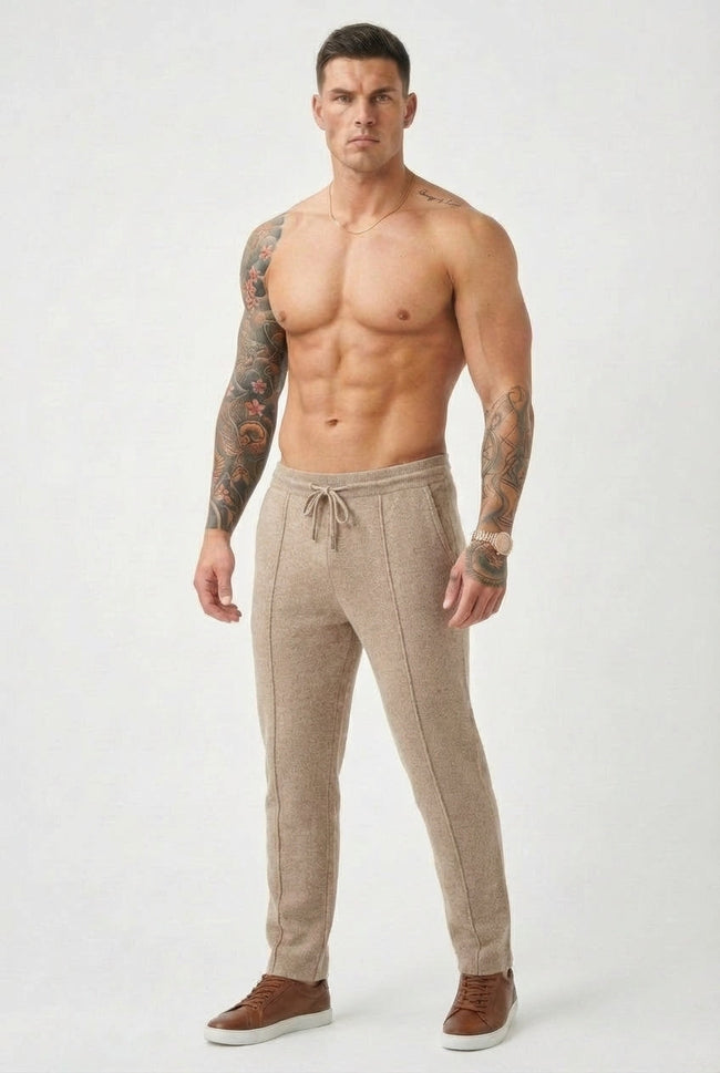 FJØRNA men's beige merino wool trousers displayed on a hanger, showcasing the soft fabric and tailored fit.