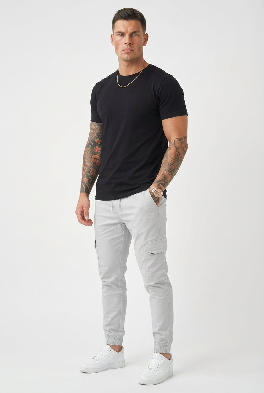 FJØRNA cargo jogger trousers in stone color with multiple pockets and relaxed fit, shown from the side.