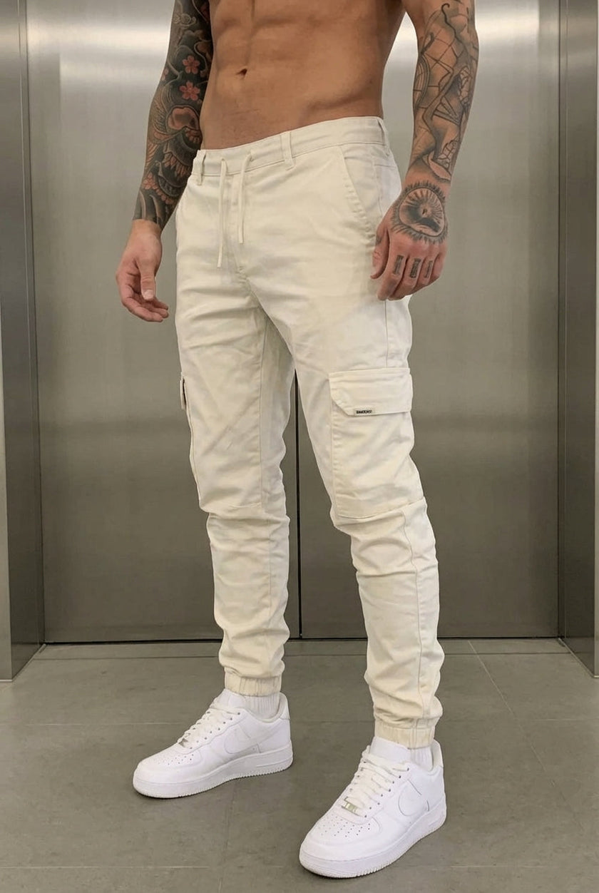 Cream cargo jogger trousers by FJØRNA, featuring relaxed fit and functional pockets, shown on a model.