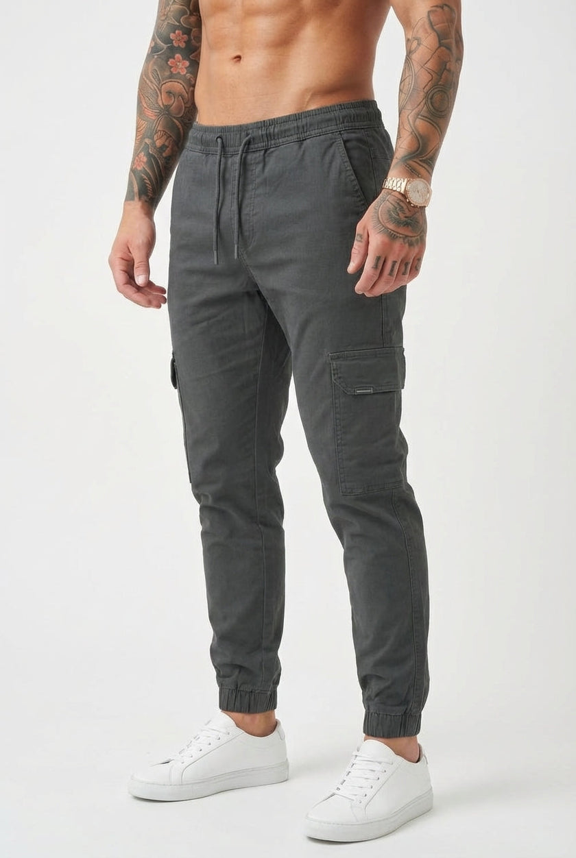 FJØRNA grey cargo jogger trousers with multiple pockets, relaxed fit, and drawstring waist, displayed on a hanger.