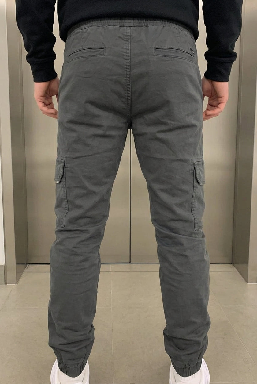 FJØRNA grey cargo jogger trousers with multiple pockets, relaxed fit, and elastic cuffs, displayed on a model.