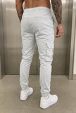 FJØRNA Cargo Jogger Trousers in stone color, featuring relaxed fit, multiple pockets, and elastic cuffs, displayed on a model.