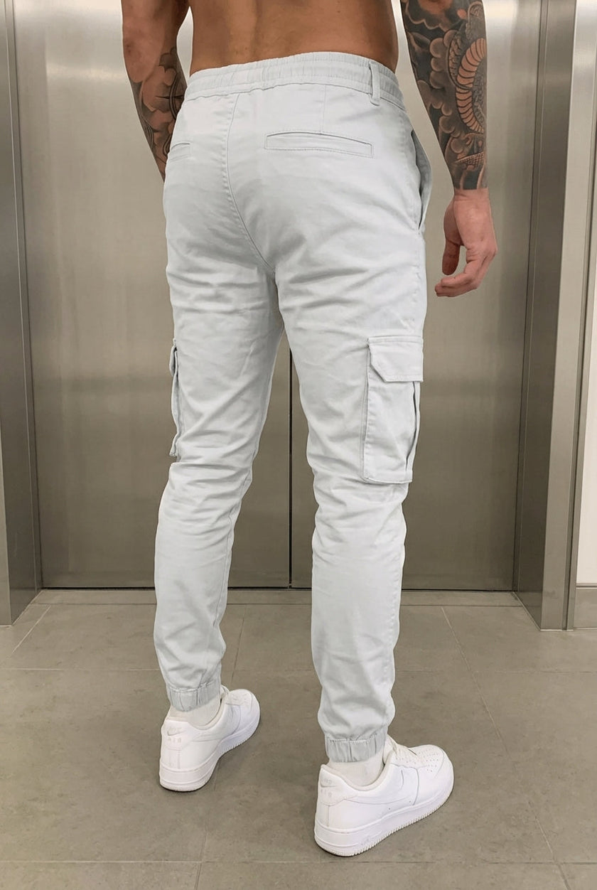 FJØRNA Cargo Jogger Trousers in stone color, featuring relaxed fit, multiple pockets, and elastic cuffs, displayed on a model.