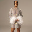 White FJØRNA sequin feather mini dress with long sleeves and sheer details, featuring sparkling sequins and feather accents.